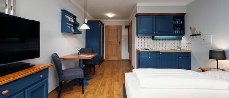 Une chambre d’hôtel de taille réduite, équipée d’une télévision, d’un coin repas, d’une kitchenette et d’un lit.