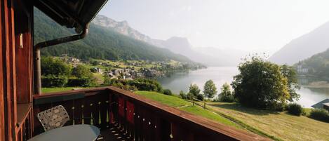 Varanda com mesa e cadeiras, vista para um lago e montanhas.