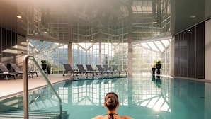 A pool area with a glass ceiling, lounge chairs, and potted plants.