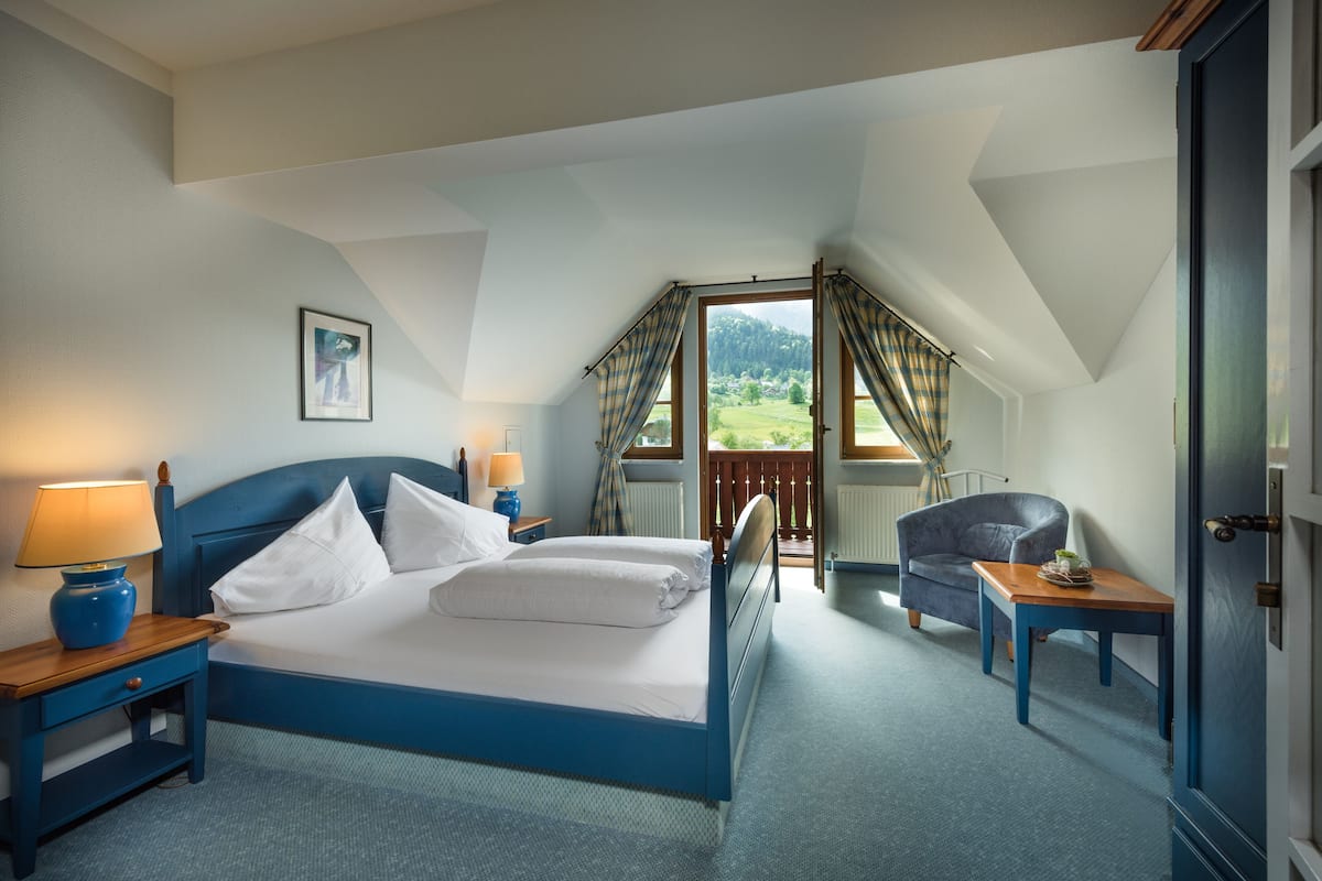 Een slaapkamer met een groot bed, twee nachtkastjes met lampen, een stoel en uitzicht op een groen landschap door een raam.