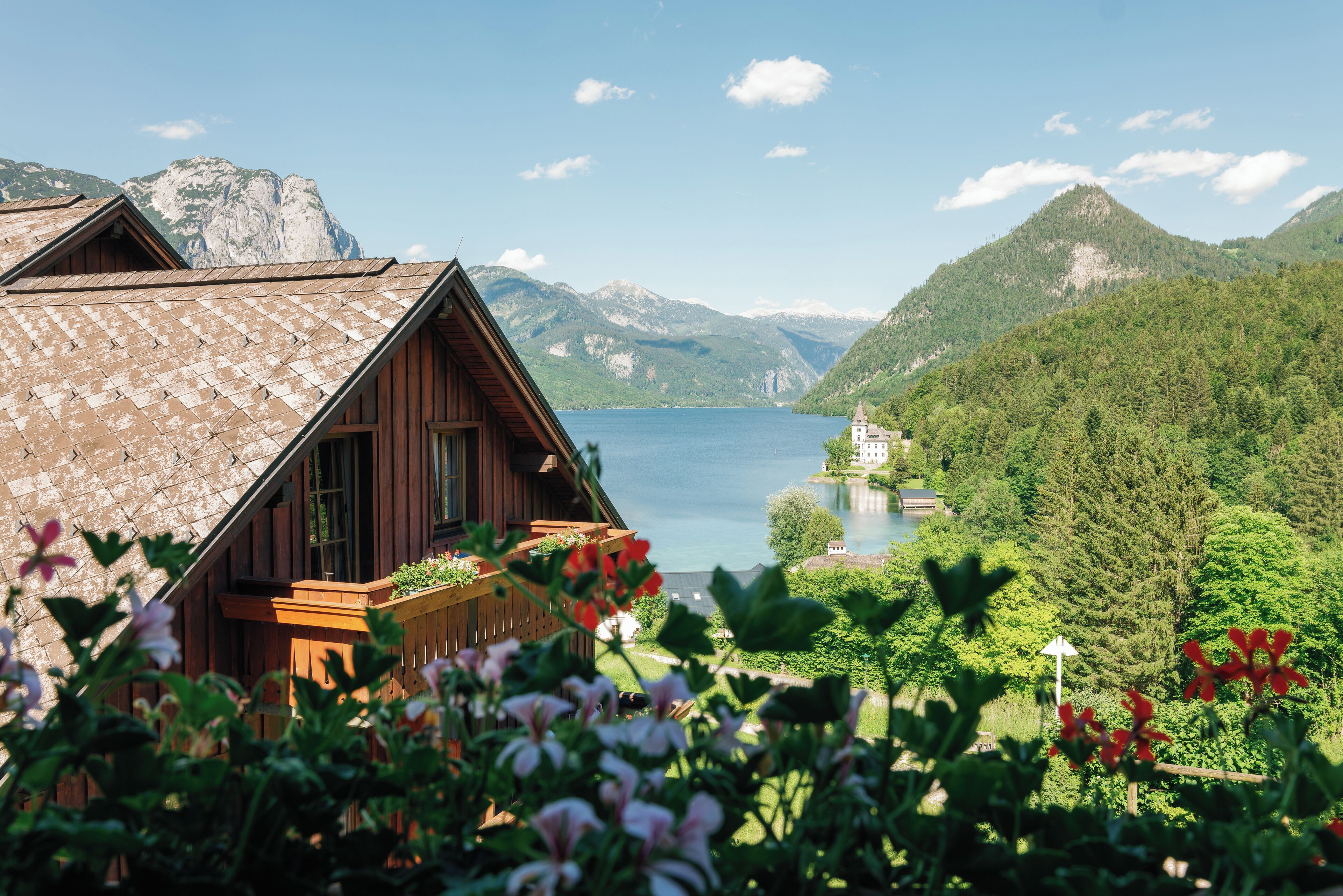 A wooden cabin with a sloped roof overlooking a lake and mountains.