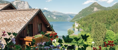 A wooden cabin with a sloped roof overlooking a lake and mountains.