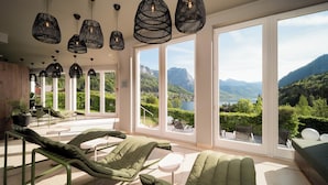 A modern room with large windows, green lounge chairs, and hanging black pendant lights.