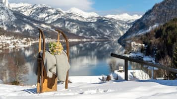 A wooden chair with a blanket and a floral arrangement in a snowy landscape with a lake and mountains in the background.