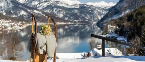 A wooden chair with a blanket and a floral arrangement in a snowy landscape with a lake and mountains in the background.