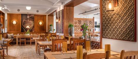 A restaurant with wooden tables and chairs, a patterned wall, and pendant lighting.