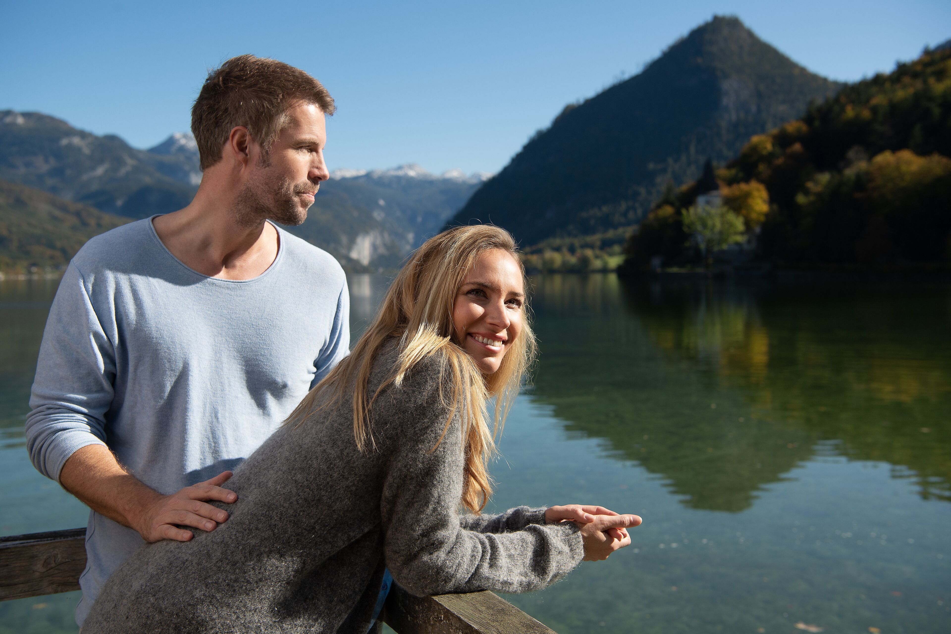 Una pareja de pie junto a un lago, con montañas al fondo.