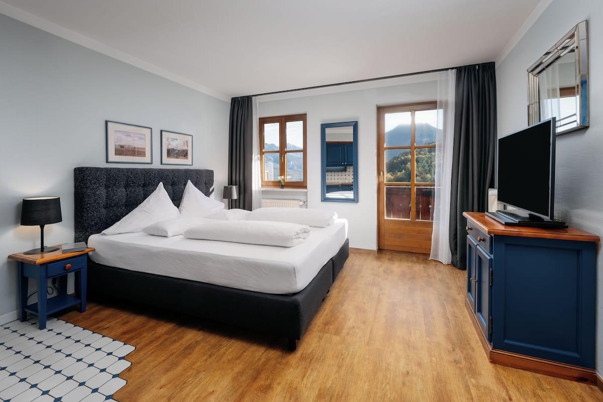 Een moderne hotelkamer met een groot bed, een flatscreen televisie en uitzicht op de bergen door de ramen.