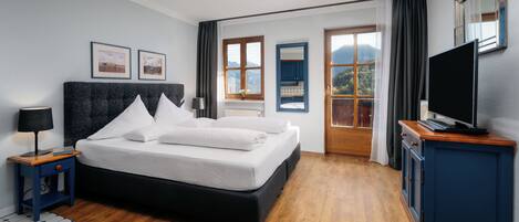 A modern hotel room with a large bed, a flat-screen TV, and a view of the mountains through the windows.