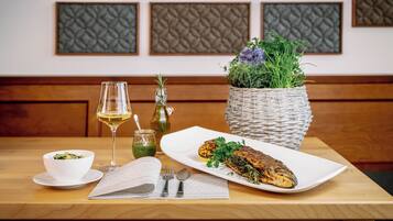 Ein Esstisch mit einem weißen Teller mit Fisch, einer Salatschüssel, einem Weinglas und einem gewebten Korb mit Grünpflanzen.