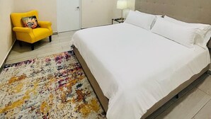 A hotel room with a large bed, a yellow armchair, a bedside table with a lamp, and a door.