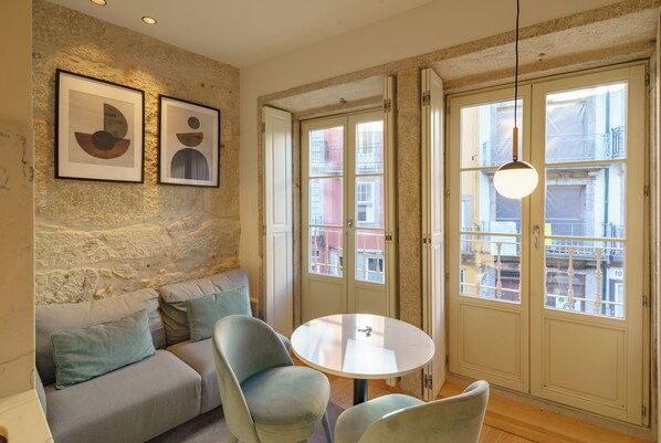 Una habitación acogedora con pared de piedra, un sofá con cojines, una mesa redonda, dos sillas y una lámpara colgante.