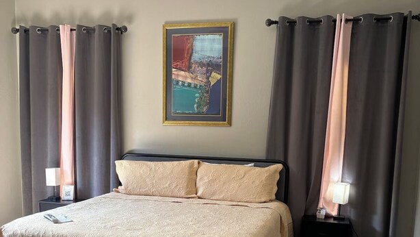 Een slaapkamer met een groot bed, twee nachtkastjes, een schilderij aan de muur en gordijnen.