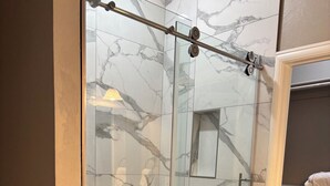 Een moderne badkamer met een douchecabine van glas, marmeren tegels en een houten vloer.