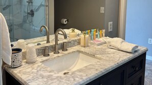 Een moderne badkamer met een grote spiegel, een wastafel met een marmeren aanrechtblad en een douche.