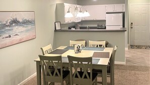 Ein Essbereich mit Tisch und Stühlen, im Hintergrund eine Küche und eine Tür zu einem weiteren Zimmer.