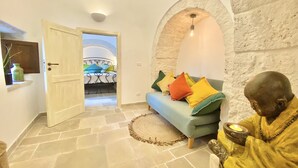 Una habitación con piso de piedra, un sofá azul con cojines de colores, una estatua y una pared de piedra con arco.