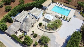 Vista aérea de una propiedad con piscina, patio cubierto y jardín ajardinado.