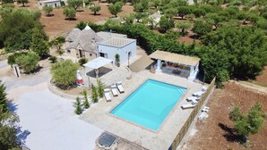 Vista aérea de una propiedad con piscina, un edificio pequeño con techo de tejas y un jardín con árboles y zona de barbacoa.
