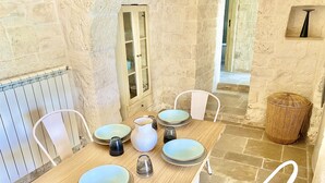 Un comedor con una mesa de madera, sillas blancas y una pared de piedra.