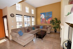 Uma sala de estar com sofá seccional, uma mesa de centro e um quadro na parede.