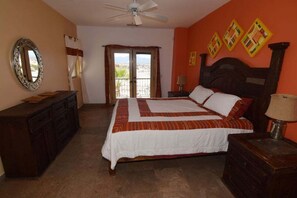 A bedroom with a bed, a dresser, a nightstand, a ceiling fan, and a window with curtains.