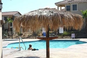 Un espace piscine agrémenté d’un parasol en chaume, d’un escalier pour accéder à la piscine et d’une personne assise au bord de la piscine.