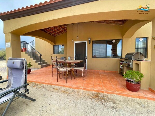 Un porche techado con mesa y sillas, una parrilla y otra silla.