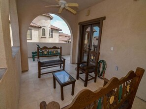 A balcony with a ceiling fan, a wooden bench, a table, and chairs.