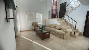 A living room with a sofa, armchair, coffee table, and a staircase with a railing.