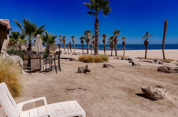 Une plage bordée de palmiers, une table avec des chaises et une chaise blanche.