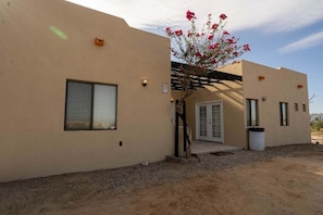 Un edificio con fachada color crema, una ventana, una puerta y un pequeño árbol con flores rosadas.