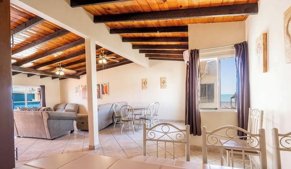 Quarto com teto de madeira, área de jantar com cadeiras de metal, sofá e mesa.