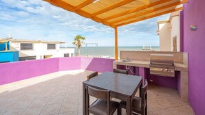A patio with a grill and table, overlooking a beach and buildings.