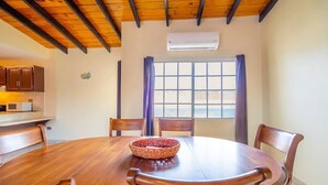 A dining area with a wooden table and chairs, a woven basket on the table, and a window with curtains.