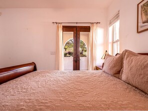 A bedroom with a bed, curtains, a window, and a door leading to an outdoor area.