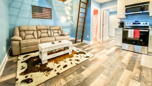 A living room with a sofa, coffee table, and a cowhide rug. A ladder is leaning against the wall. - Luxury Treehouse Eagles Nest (Clarks Hill)