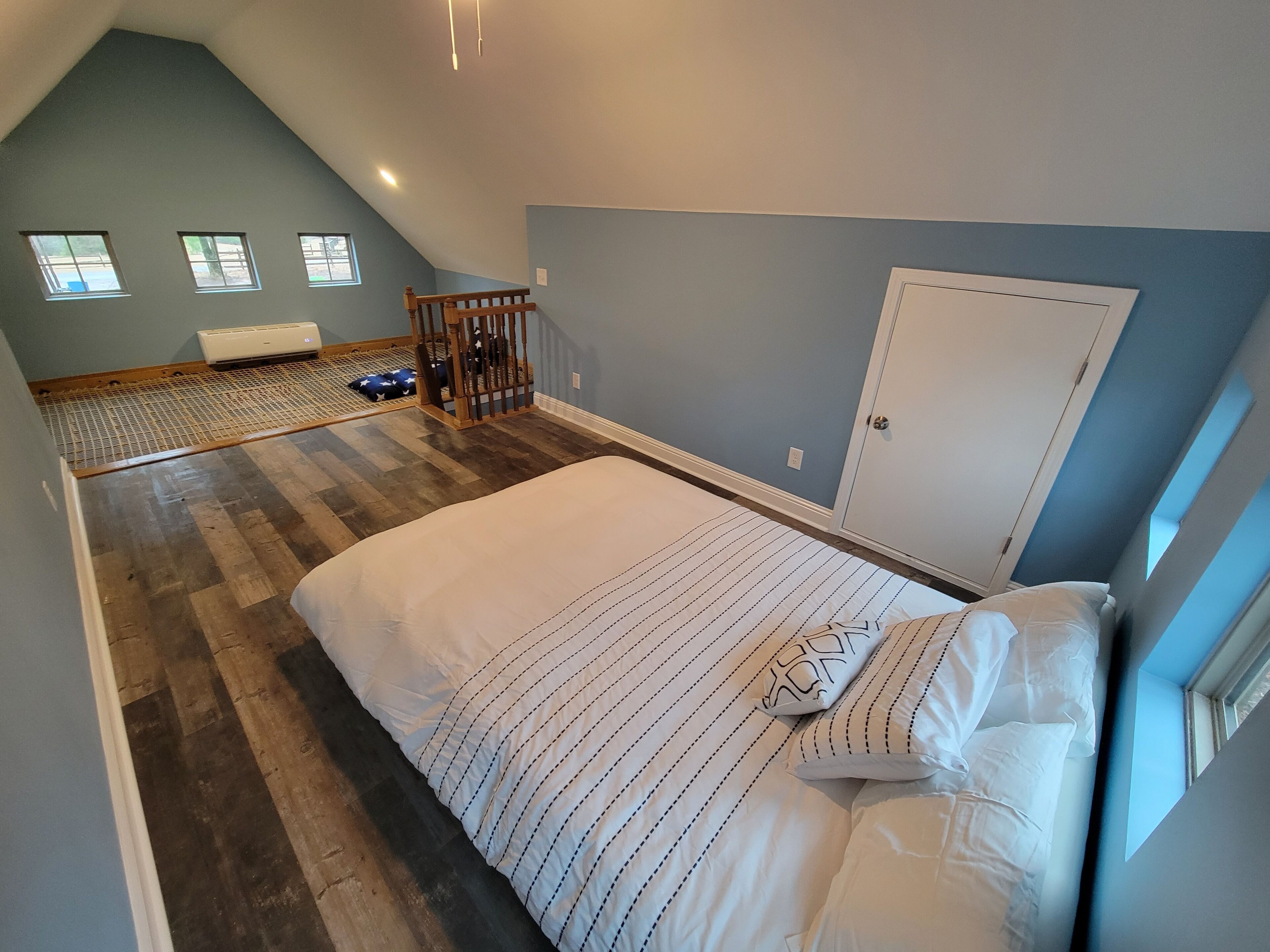 A bedroom with a sloped ceiling, a bed with striped bedding, a wooden crib, and a white door.