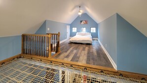 A bedroom with a sloped ceiling, a bed, a window, and a wooden railing. - Luxury Treehouse Eagles Nest (Clarks Hill)