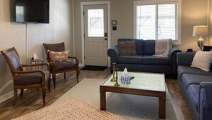 A living room with a flat-screen TV, a ceiling fan, a sofa, a coffee table, and a door with a window. - NEAR BRAZOS COUNTY EXPO CENTER. ENJOY FRESH AIR AND STARRY NIGHTS. (Bryan)