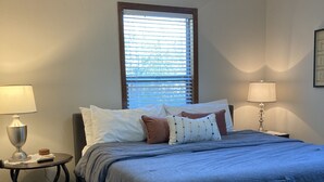 A bedroom with a bed, two bedside tables, a window with blinds, a ceiling fan, and a patterned rug. - NEAR BRAZOS COUNTY EXPO CENTER. ENJOY FRESH AIR AND STARRY NIGHTS. (Bryan)