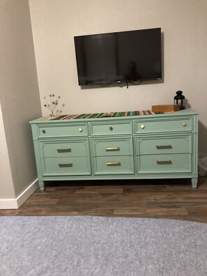 A teal dresser with drawers, a flat-screen TV mounted above it, and a small plant on the dresser.