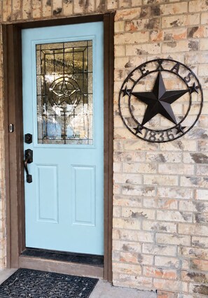 A light blue door with a decorative glass panel and a metal star sign on the wall. - Steps to Brazos County Expo 2 Acres + Fire Pit  Sleeps 9 (Bryan)