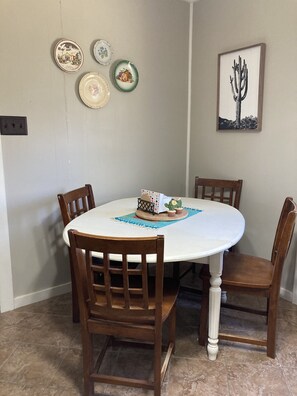 A dining table with four wooden chairs, a white tablecloth, and a cactus centerpiece.