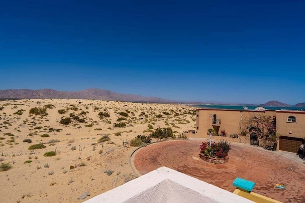 Un paysage désertique avec un bâtiment doté d’une allée incurvée et d’un petit jardin.