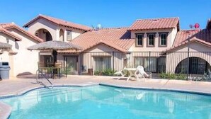 A swimming pool with a clear blue water, a patio area with chairs, and a building with a tiled roof. - Condo 21-1 El Dorado Ranch (San Felipe)