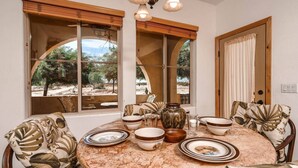 A dining area with a round table, chairs, and a view of an outdoor landscape through large windows. - Condo 21-1 El Dorado Ranch (San Felipe)