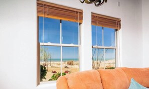 A room with two large windows offering a beach view, a white wall, and an orange sofa.