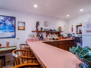 A kitchen with a long countertop, wooden chairs, a refrigerator, and various kitchen appliances. - La Hacienda Condo Seven (San Felipe)