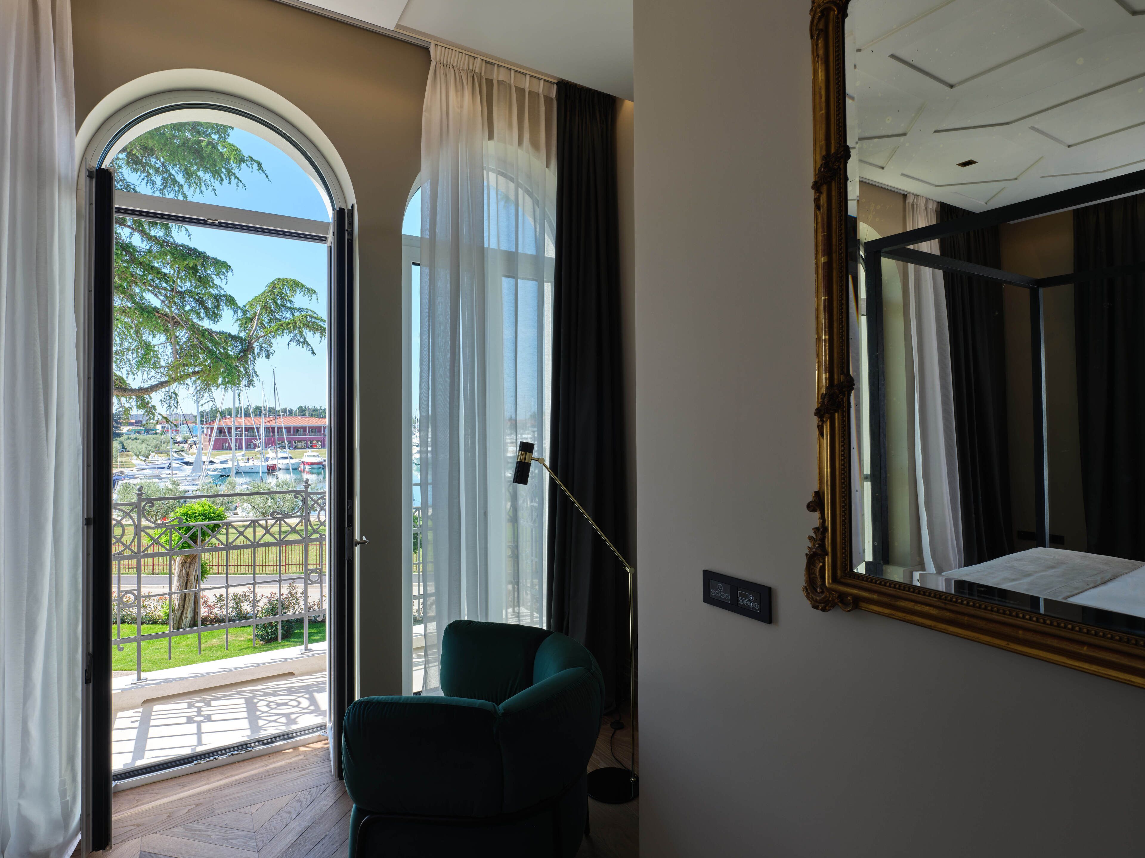 Habitación con vistas a un puerto deportivo, una silla verde, un espejo grande y un techo con diseño geométrico.